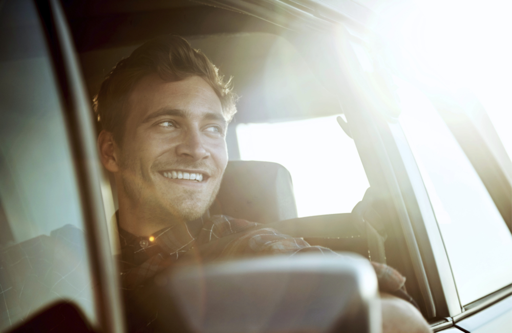 man lachend in de auto met zon