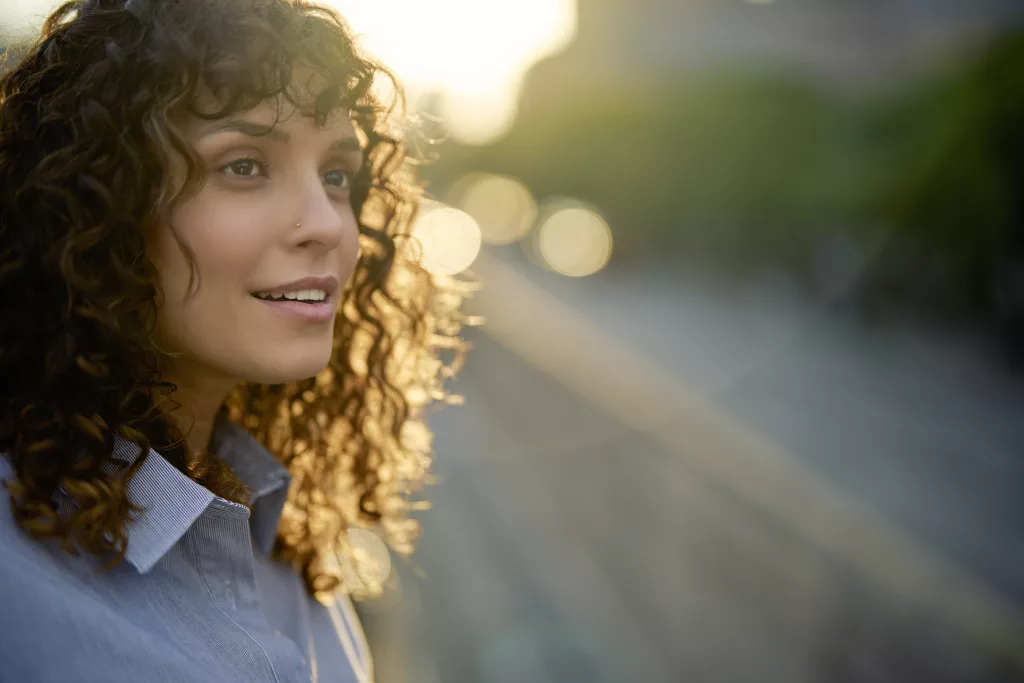 vrouw met krullen en neuspiercing die geinspireerd kijkt met blur achtergrond